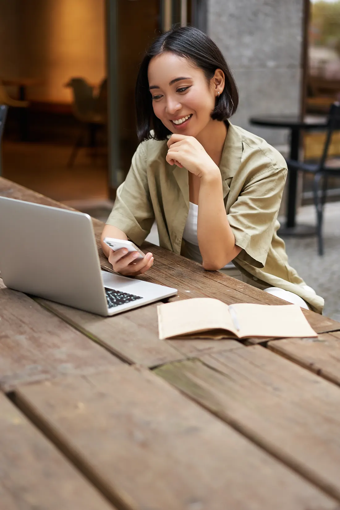 A learner checking her phone beside a laptop and an open notebook